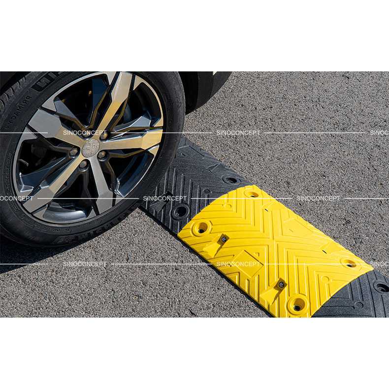 Car wheel driving over a 5cm black and yellow safety speed bump on asphalt road.