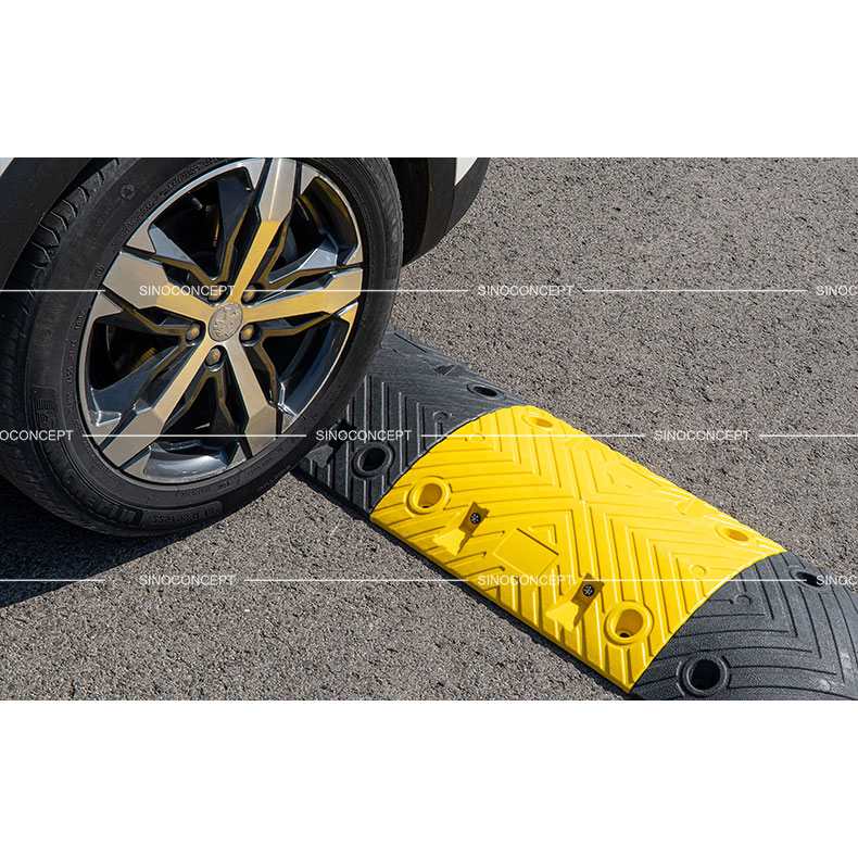 Car wheel driving over a 5cm black and yellow traffic speed bump on asphalt road.