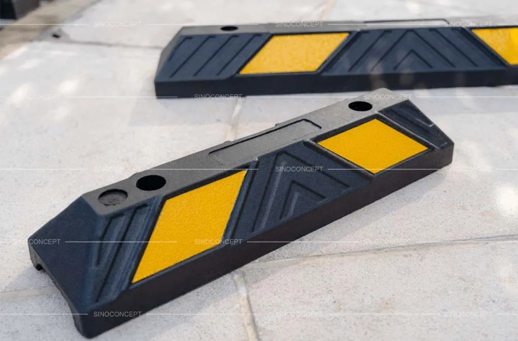 Two black wheel stops made of vulcanised rubber with yellow reflective films for car park management.