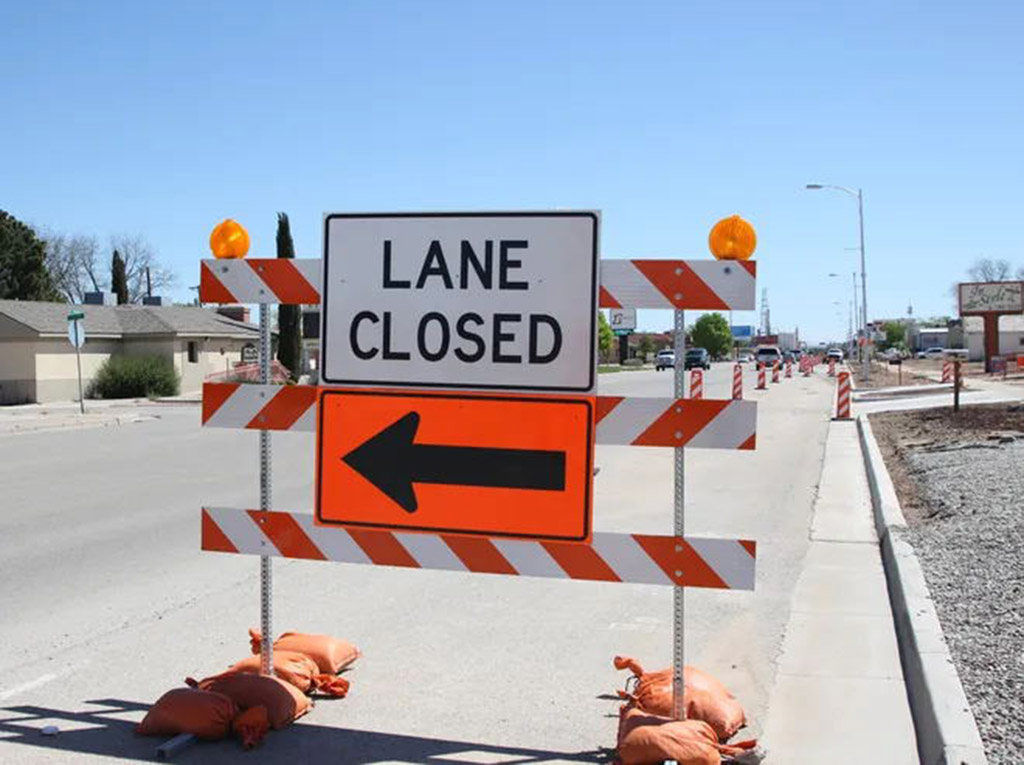 Orange sandbags used to stabilize construction warning signs on the road