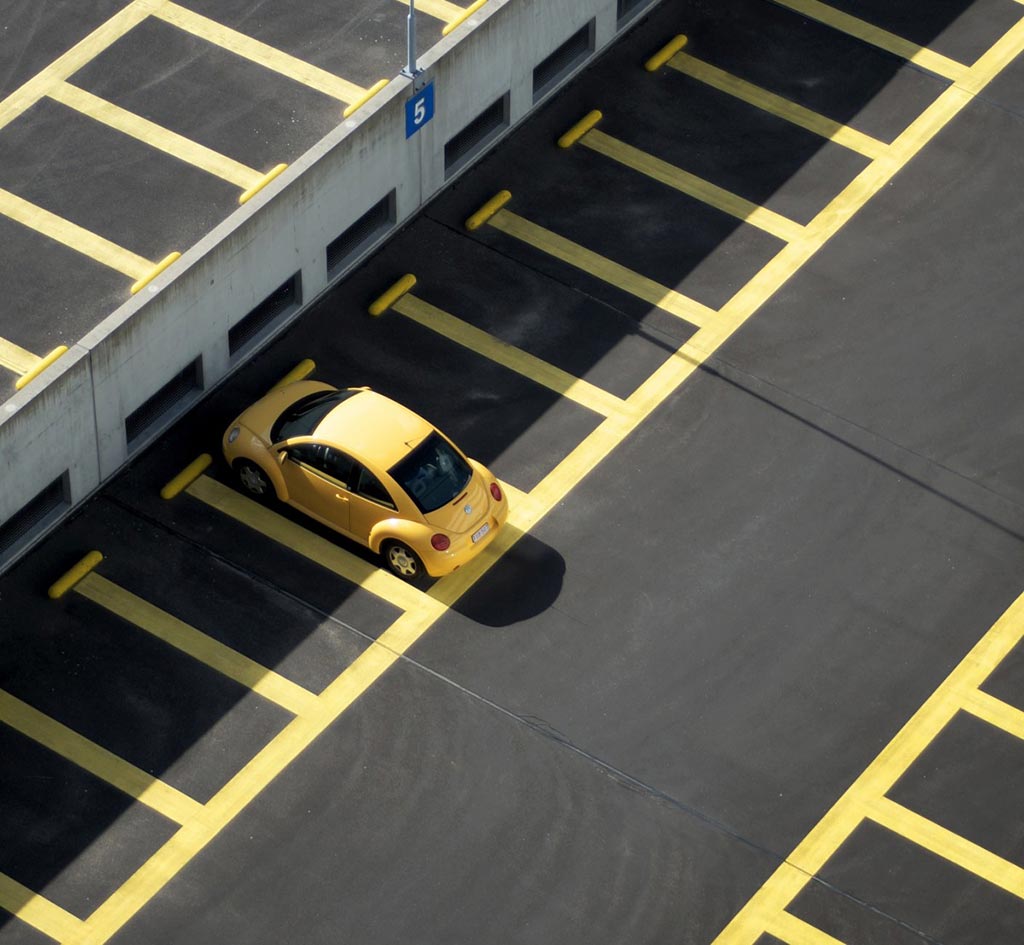 Yellow parking wheel stops are installed in a big outside parking lot with yellow markings for well-organized parking management