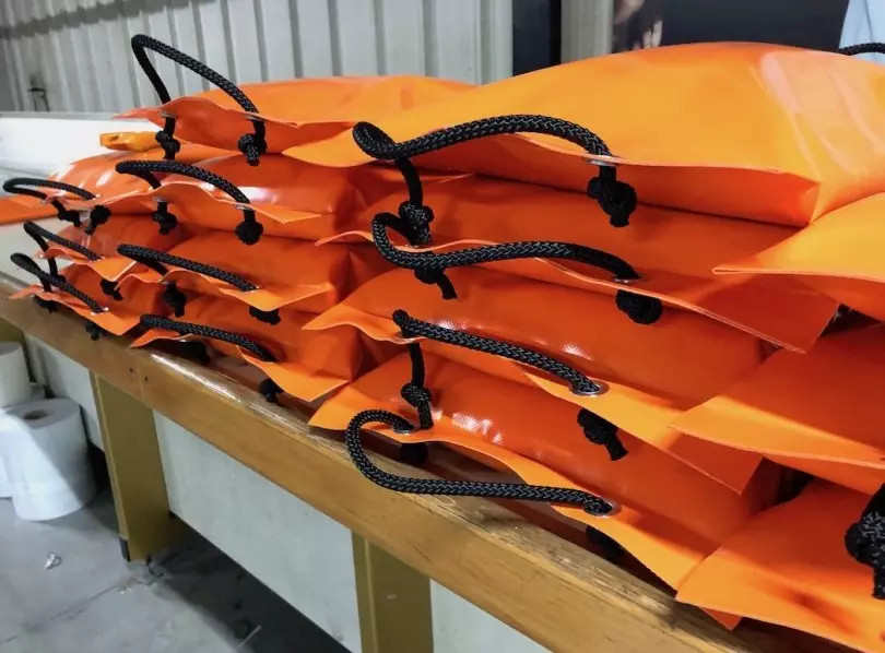 Many orange PVC sandbags are stacked together.