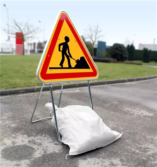 A white polypropylene sandbag holds down a traffic sign to prevent it from falling down.