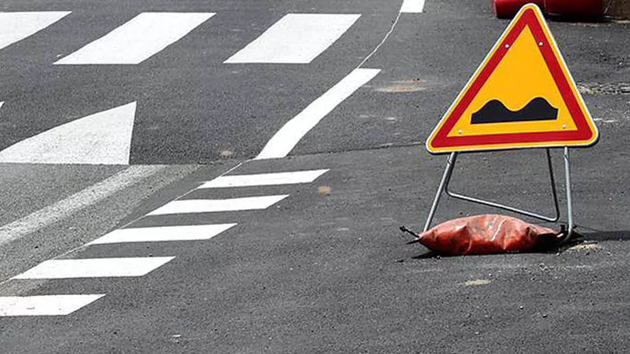 An orange sandbag holds down a traffic sign on the road to prevent it from falling down.