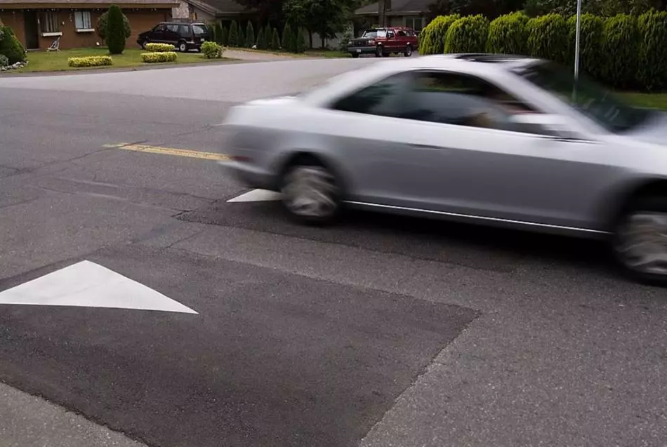 A silver car is driving over asphalt speed cushions.