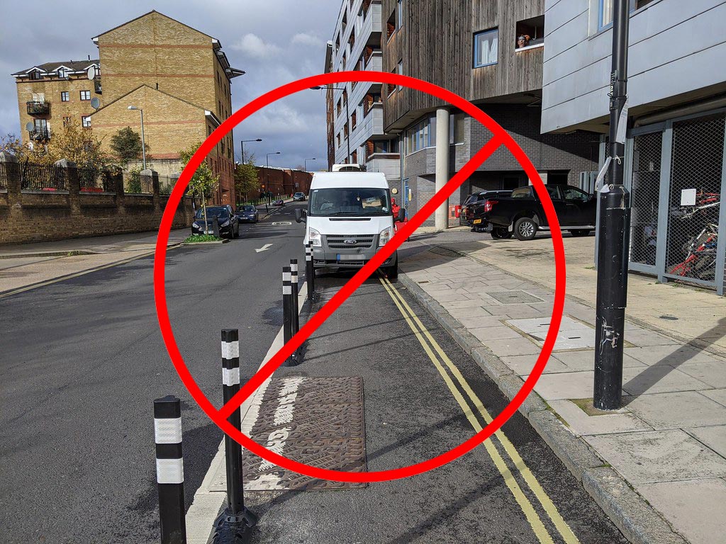 A car is parked wrongly in a cycle lane that is separated by a line of black posts and white road markings