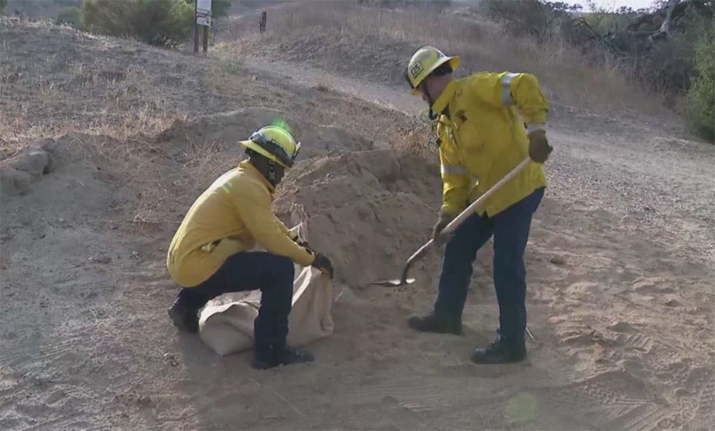 Two workers are filling sandbags with dirt