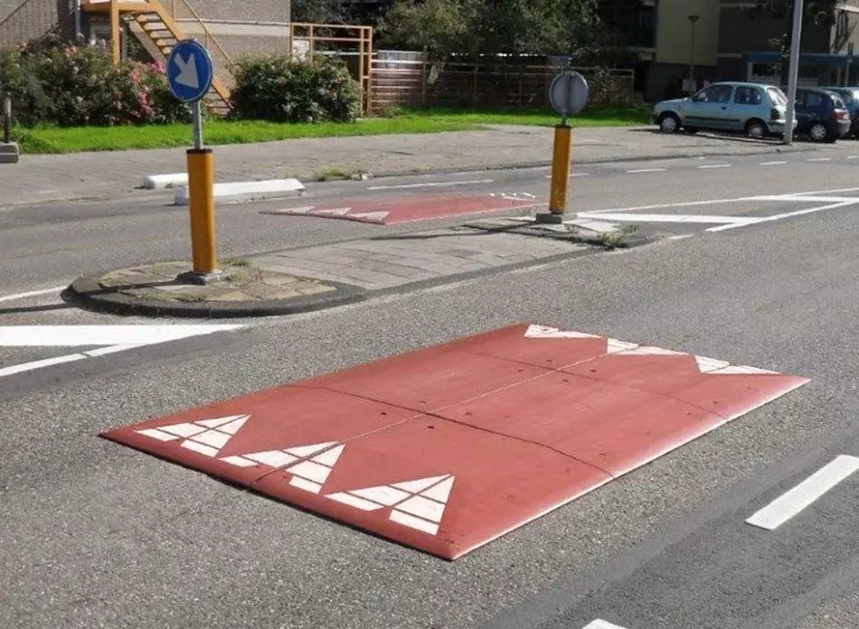 A Europe red rubber road speed cushion is mounted on the road as a speed traffic-management tool.