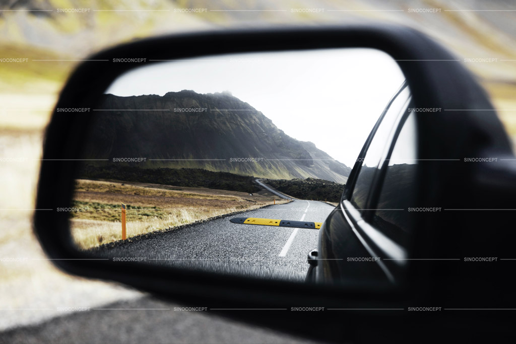 A speed bump on the road shown in the rear mirror of a car