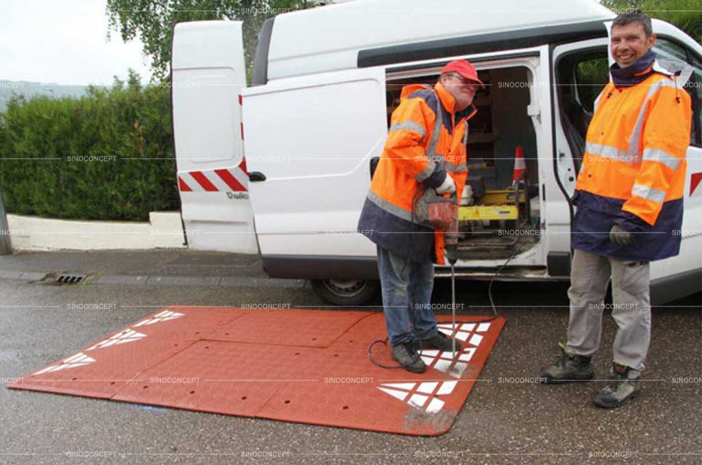 Two workers are installing a rubber speed cushion on the road