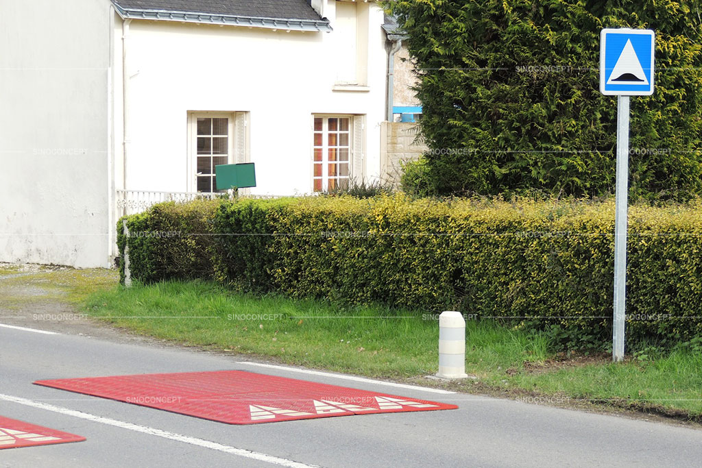 Red and white speed cushions put on the road for traffic calming purposes with a traffic sign near it