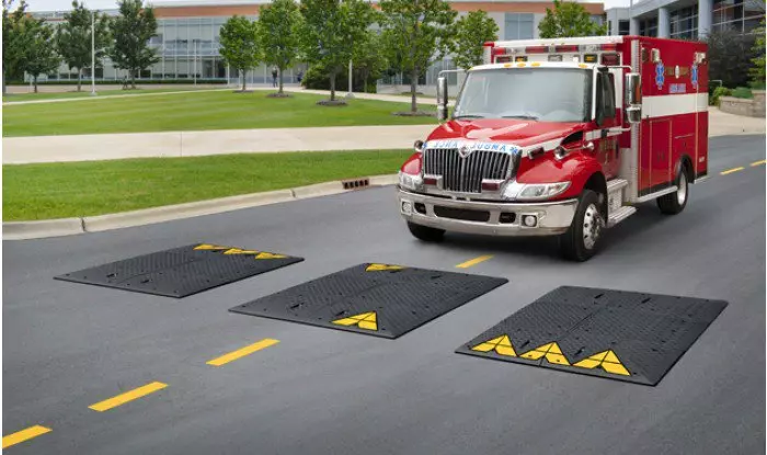 An emergency vehicle is about to pass over the black speed cushions with yellow markings without any hurdle.