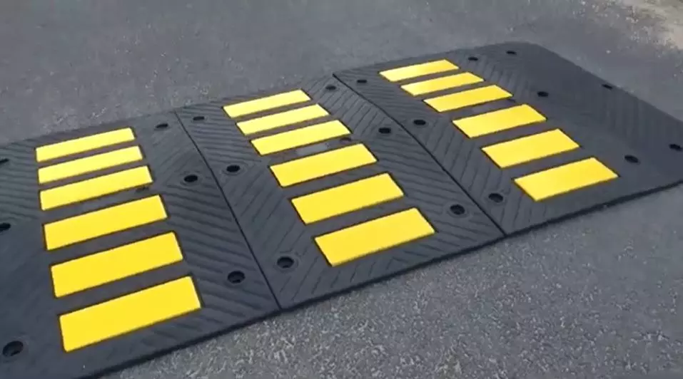 Speed hump, also called road hump, made of black rubber and yellow glass bead reflective tapes for traffic-calming purposes.