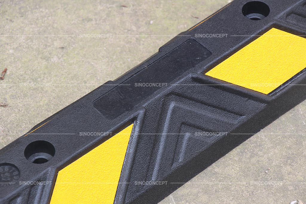 A black rubber wheel stopper pasted with yellow reflective films for car parking management