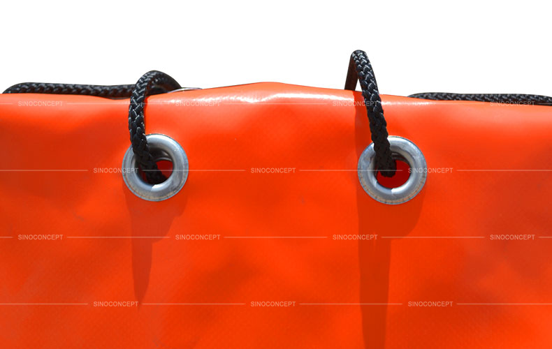 Aluminium eyelets and black strings accessories used on orange PVC sandbags for traffic safety management