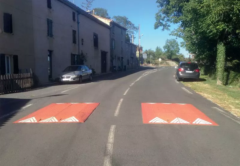 Two red rubber road cushions are mounted on the road as traffic-calming measures.