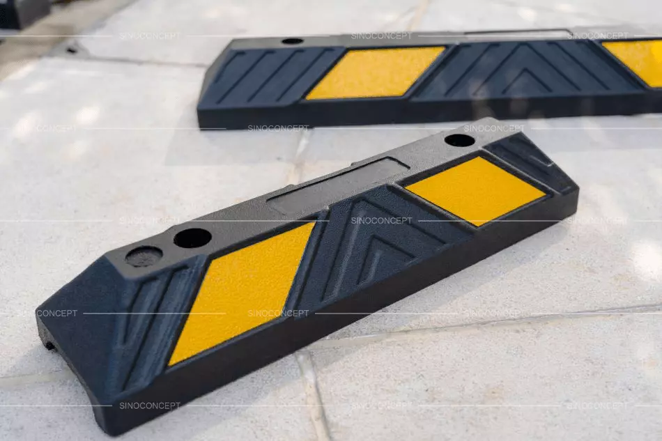 Black rubber parking bumpers with yellow reflective films to stop vehicles in parking spaces.