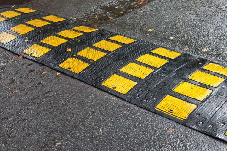 A black and yellow speed hump on the road that does not block rain or stormwater.
