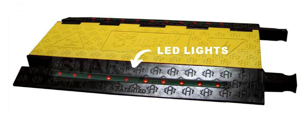 A black and yellow cable ramp with LED lights on both sides to warn people.