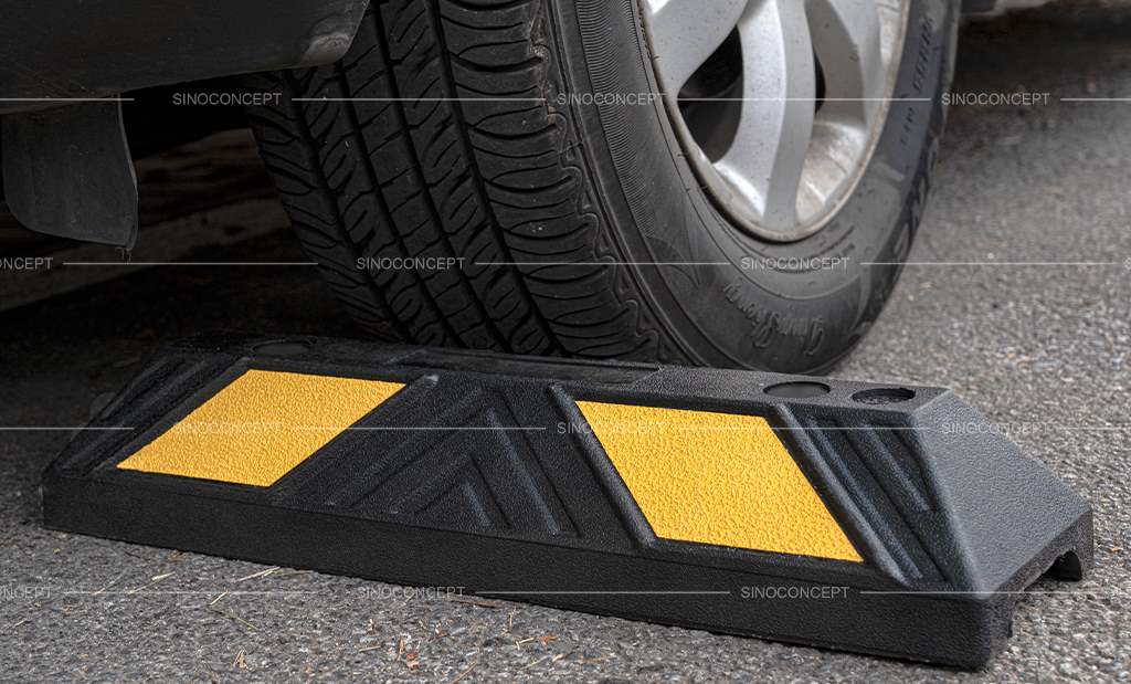 A black parking bumper with yellow reflective films is mounted on the ground to ensure safe parking.