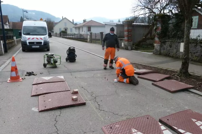 Two men are installing red rubber speed cushions.
