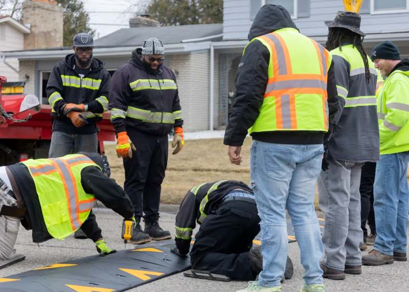 Some people are installing a speed hump with bolts and a drilling machine.