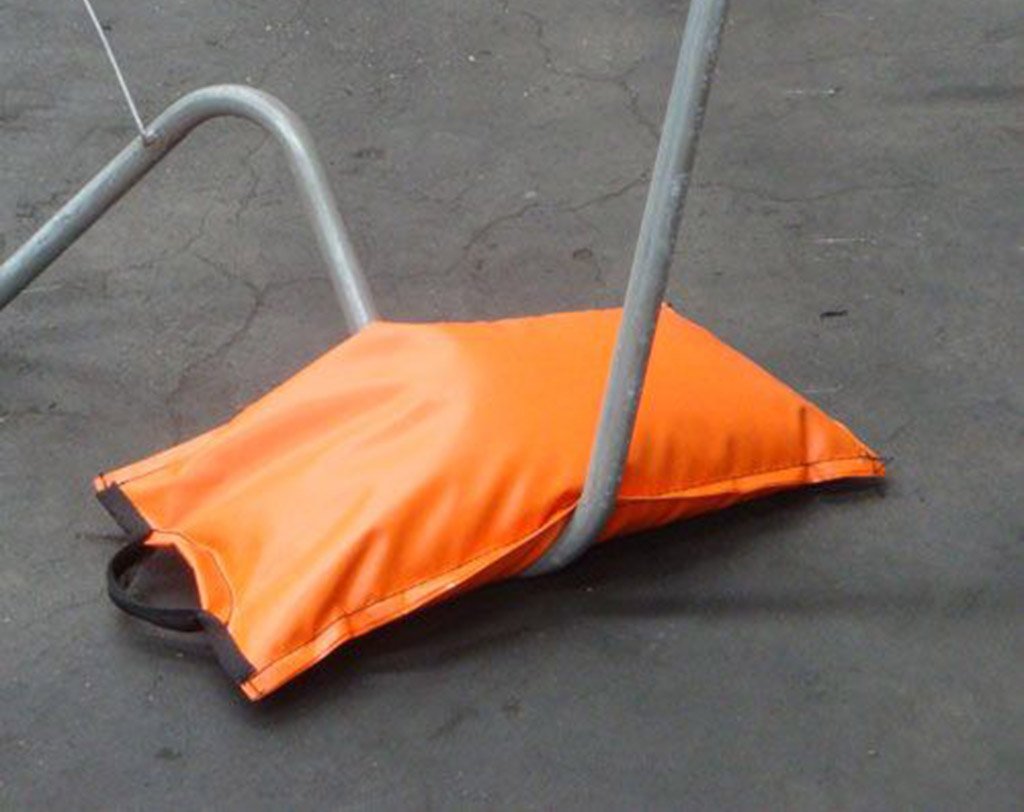 A traffic sandbag coloured in orange with a black string, is used to hold down a traffic sign