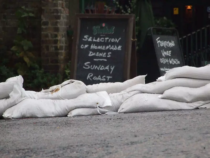 Many white polypropylene sandbags are stacked together on the ground.