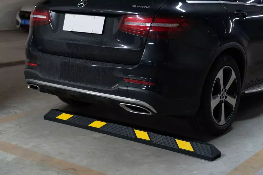 A black car is parked inside a parking space with the help of an 1830mm rubber wheel stop.
