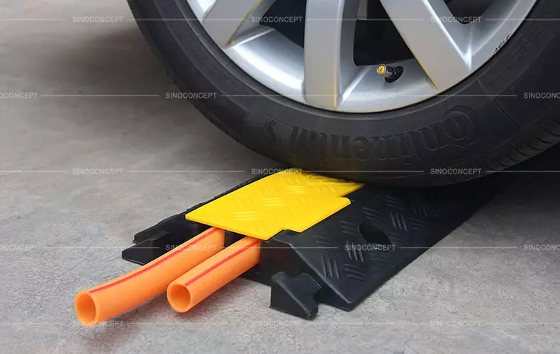 A 2-channel cable guard, also called an outdoor cable protector, is made of black recycled rubber with yellow covers, with one orange hose in each channel.