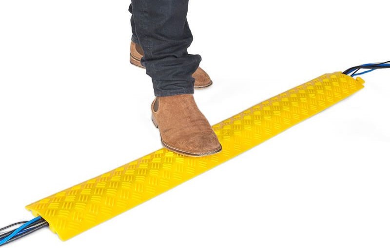 A person is walking over a yellow drop-over cable protector on the floor, which is used for protecting wires.