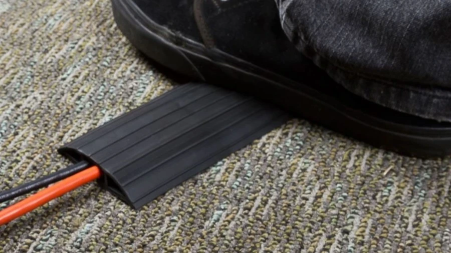 A man is stepping on a black floor cord cover which protected the cords.