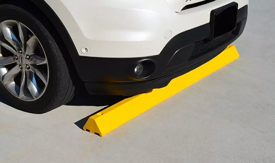 A yellow parking bumper made of recycled plastic is mounted on the ground for parking safety.