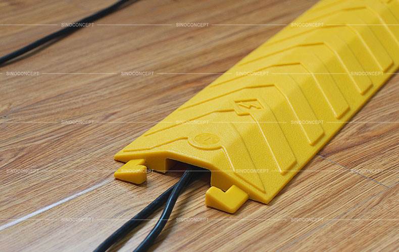 A bright yellow drop-over cable cover made of polyurethane on the floor to protect two black wires.