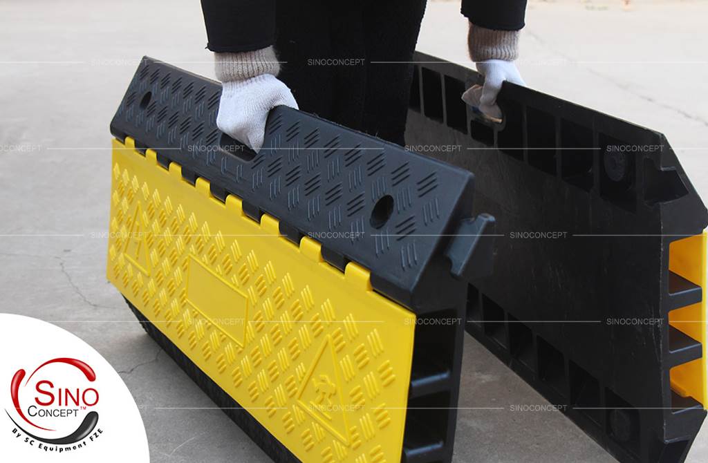 A person is holding two parts of black and yellow outdoor cable ramps made of rubber.