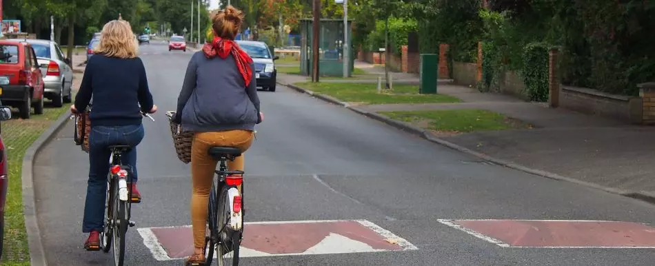 Two cyclists are passing by the red concrete speed cushions with white markings.