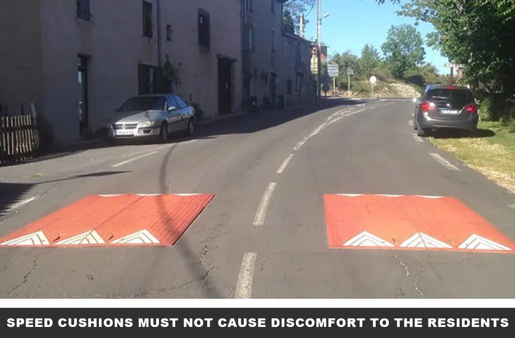 Two red rubber speed cushions with white reflective tapes mounted on the road next to the building as traffic-calming measures.