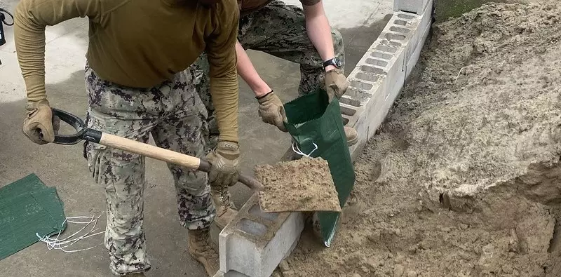 A dark green sandbag is being filled with sand.