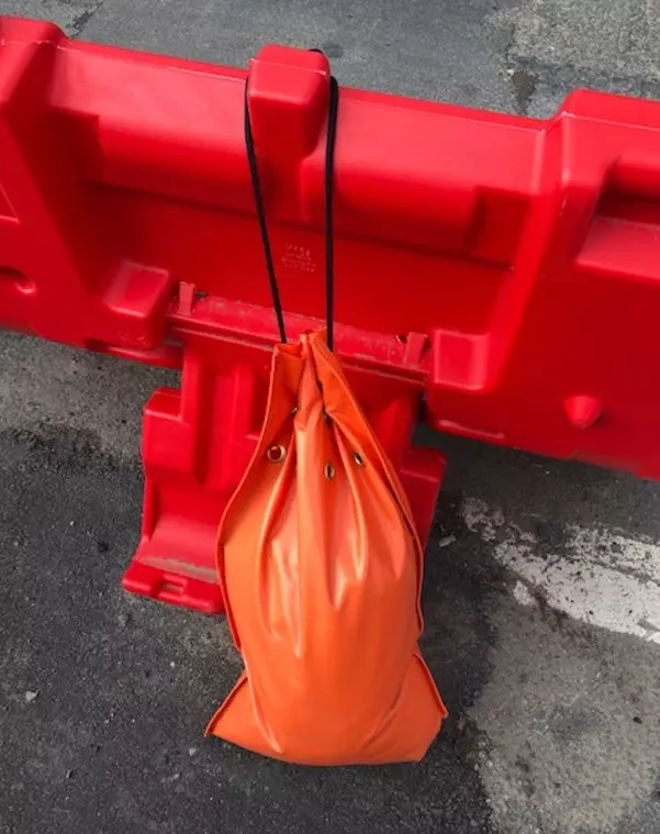 An orange sandbag tied to a red plastic new jersey barrier.