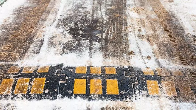 A black and yellow speed hump in the snow.