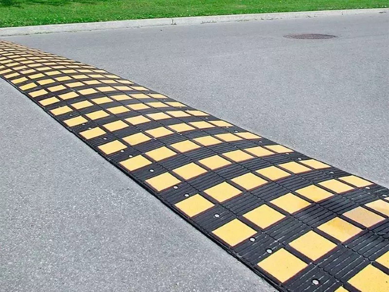 A black and yellow speed hump is mounted on the road for traffic safety management.
