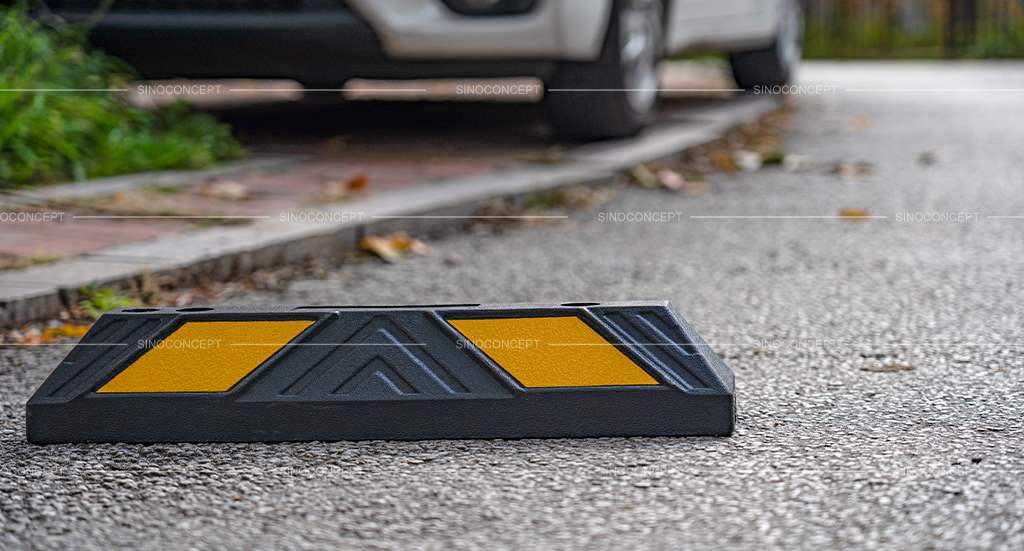 A black wheel stop made of rubber with yellow reflective films placed near a car.