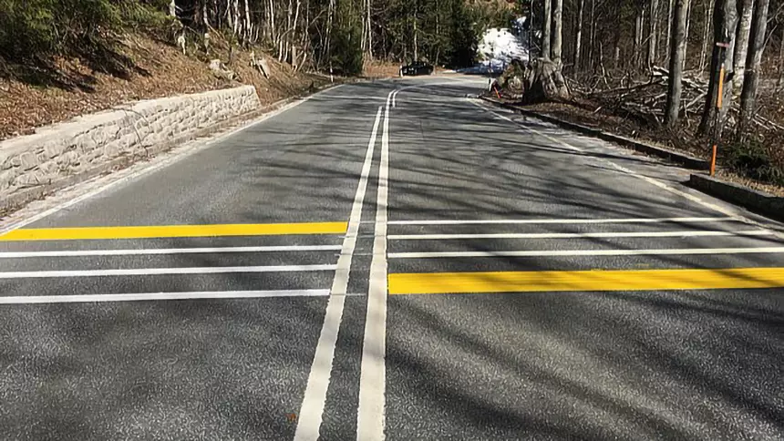 White and yellow rumble strips on the road to alert drivers to limit speed.