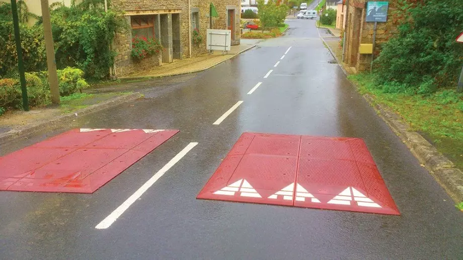 Two red rubber speed cushions are mounted on the road for traffic safety management.