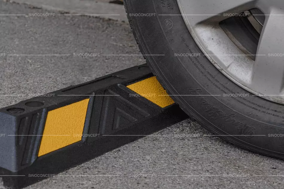 A 550mm black and yellow parking block on the ground nearby the wheels of a car.