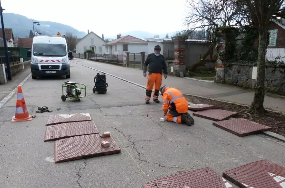 Two men are installing red rubber speed cushions on the ground.