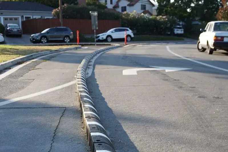 Black rubber curb with white stripes mounted on the ground as curbing solutions.