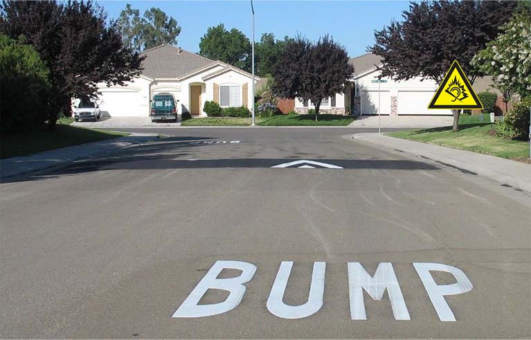 A black asphalt speed bump with white markings on the road for traffic-calming purposes.