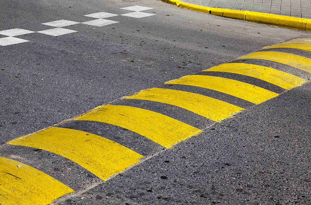 An asphalt speed bump with yellow markings for reducing speed.