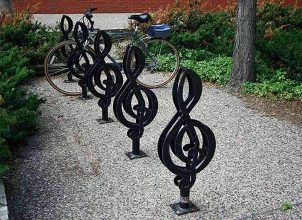 Several black bicycle racks shaped like musical notes are installed on the ground.